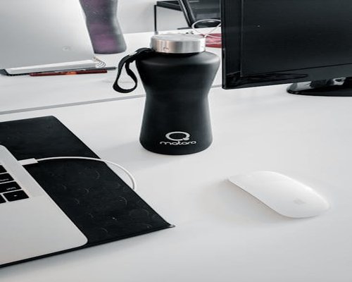 An elegant reusable water bottle standing next to a contemporary computer setup inside a clean modern workspace