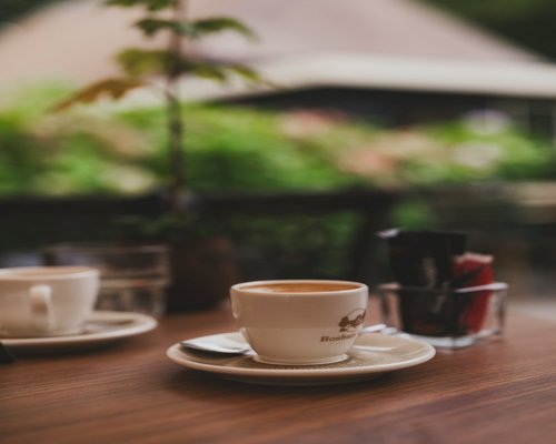 A close-up shot of a white porcelain coffee cup served alongside a tall sparkling glass of mineral water on a cafe terrace table