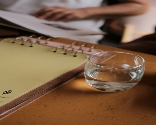 A clean glass of fresh water standing on a modern wooden office desk next to a planner
