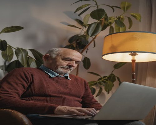 A mature man sitting comfortably in a well-lit living room armchair during a quiet evening